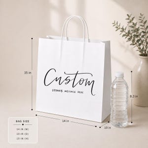 May include: A white paper shopping bag with a custom design, featuring the word "Custom" in elegant script. The bag is 14 inches wide, 10 inches deep, and 15 inches high, with white handles. The text "OPTIONAL MESSAGE HERE" is below the word "Custom".