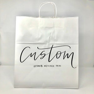 May include: White paper shopping bag with twisted paper handles. The word "Custom" is written in black script across the front, with "Optional Message Here" below it. The bag is designed for personalization.