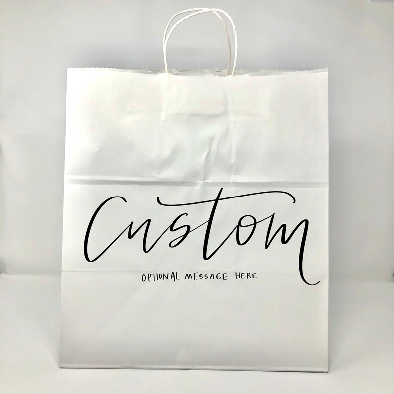 May include: White paper shopping bag with twisted paper handles. The word "Custom" is written in black script across the front, with "Optional Message Here" below it. The bag is designed for personalization.