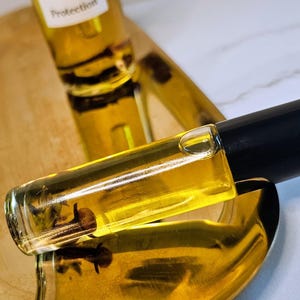 May include: Two bottles of essential oil on a gold tray. The larger bottle has a dropper and a label that says "Protection". The smaller bottle is a roll-on.