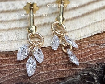 Puede incluir: Un par de pendientes dorados con gemas claras, talladas en marquesa, colgantes. Los pendientes tienen un diseño de poste y tachuela con un pequeño detalle floral. La marca "STAR JEWELLERY" está impresa en la superficie de madera.