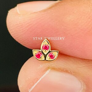 Peut inclure: Bague de nez en or avec un motif de lotus et trois pierres précieuses rouges. STAR JEWELLERY est écrit en arrière-plan.