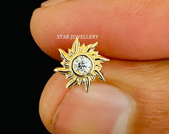 May include: Gold nose ring with a sun design and a clear stone in the center. STAR JEWELLERY is written in the background.