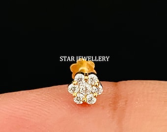 May include: A gold nose ring with a flower design set with clear cubic zirconia stones.  The ring is on a finger.