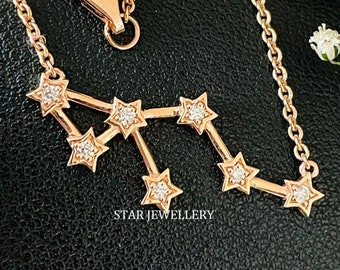 May include: A delicate gold necklace with a constellation design featuring small sparkling diamonds. The necklace is on a black background with a small bouquet of white flowers.