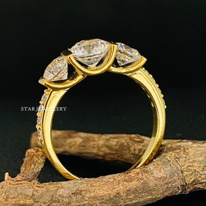 May include: A gold ring with three large, clear, round gemstones set in a prong setting. The ring is on a brown wooden surface.