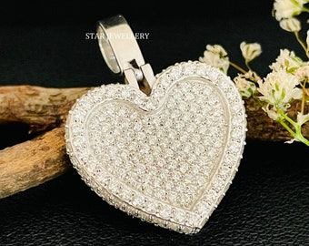 May include: A silver heart-shaped pendant with a detailed design of small, sparkling stones. The pendant is on a silver chain and is surrounded by white flowers.