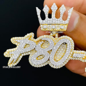 May include: A gold pendant with a crown on top and the number "780" in large, stylized letters. The pendant is covered in small, clear diamonds.