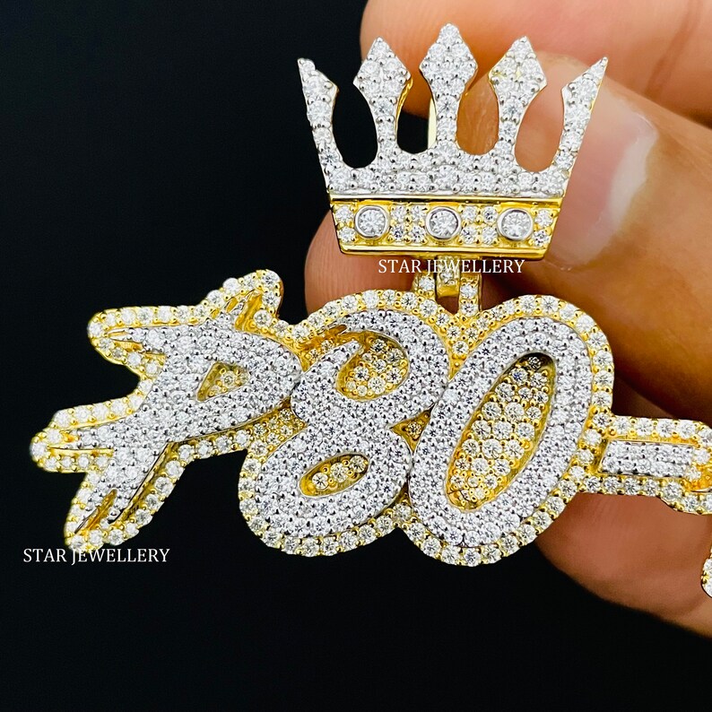 May include: A gold pendant with a crown on top and the number "780" in large, stylized letters. The pendant is covered in small, clear diamonds.
