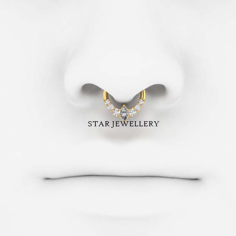 May include: A gold nose ring with a marquise-shaped center stone and round stones set in a curved line on either side. The ring is worn in a nose piercing. The text "STAR JEWELLERY" is visible below the ring.