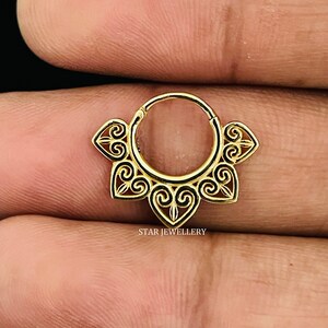 May include: Gold hoop earring with a delicate, intricate design featuring a series of connected hearts and swirls. The earring is made of a thin, circular band with a decorative, openwork design.