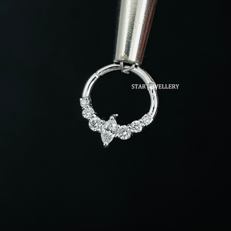 May include: A silver hoop earring with a marquise-shaped diamond and smaller round diamonds set in a row. The earring is held by a tool with the text "STAR JEWELLERY" visible.