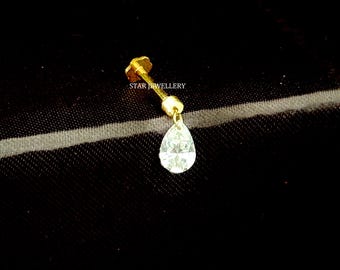 May include: A gold-colored nose stud with a teardrop-shaped, clear gemstone. The stud has a small, flower-shaped backing and a slender post. The text "STAR JEWELLERY" is printed on the image.