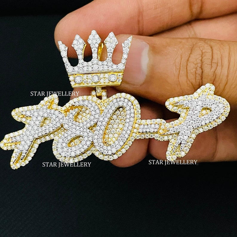 May include: A gold pendant with a crown on top and the number "7307" set with diamonds. The pendant is held in a hand. The text "STAR JEWELLERY" appears twice on the image.