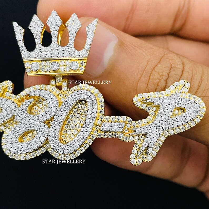 May include: Gold pendant with a crown on top and the numbers "807" set with diamonds. The pendant is held in a hand. The text "STAR JEWELLERY" appears twice on the pendant.
