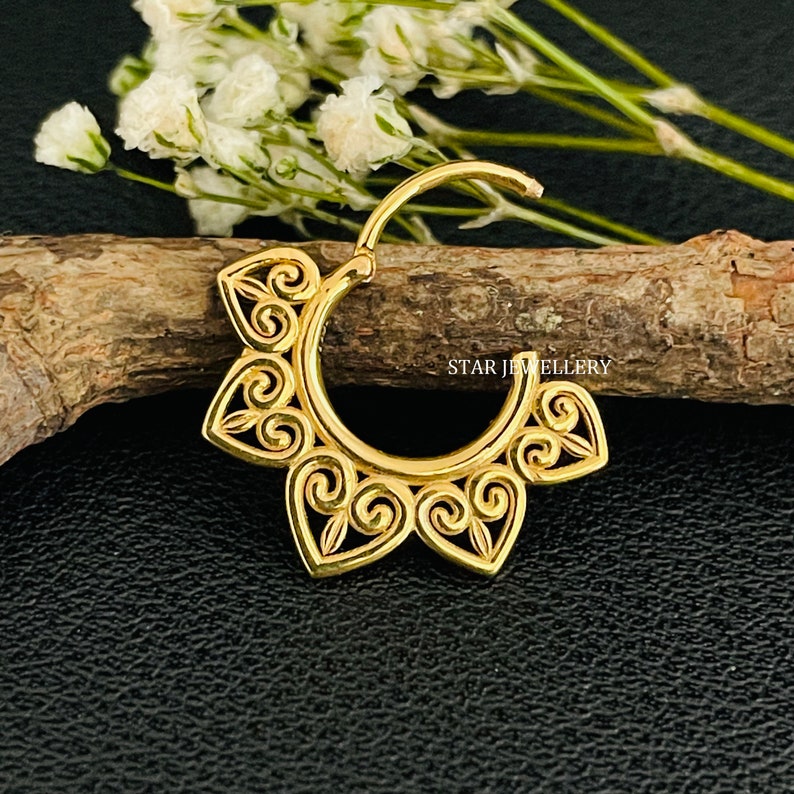 May include: Gold-toned hoop earring with a decorative, intricate design featuring a repeating swirl pattern. The earring is made of metal and has a hinged closure.