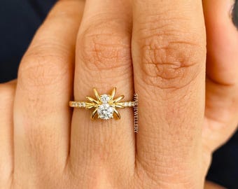May include: A gold ring featuring a unique spider design. The ring has a large, round, clear gemstone in the center, with smaller gemstones and decorative elements. The ring is on a finger.