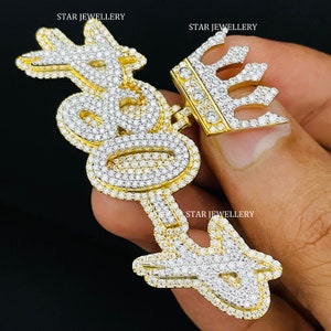 May include: A gold pendant with a crown and the word "Boss" spelled out in diamonds. The pendant is on a chain and is being held by a hand.