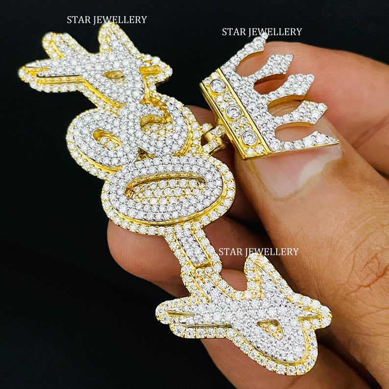 May include: A gold pendant with a crown and the word "Boss" spelled out in diamonds. The pendant is on a chain and is being held by a hand.