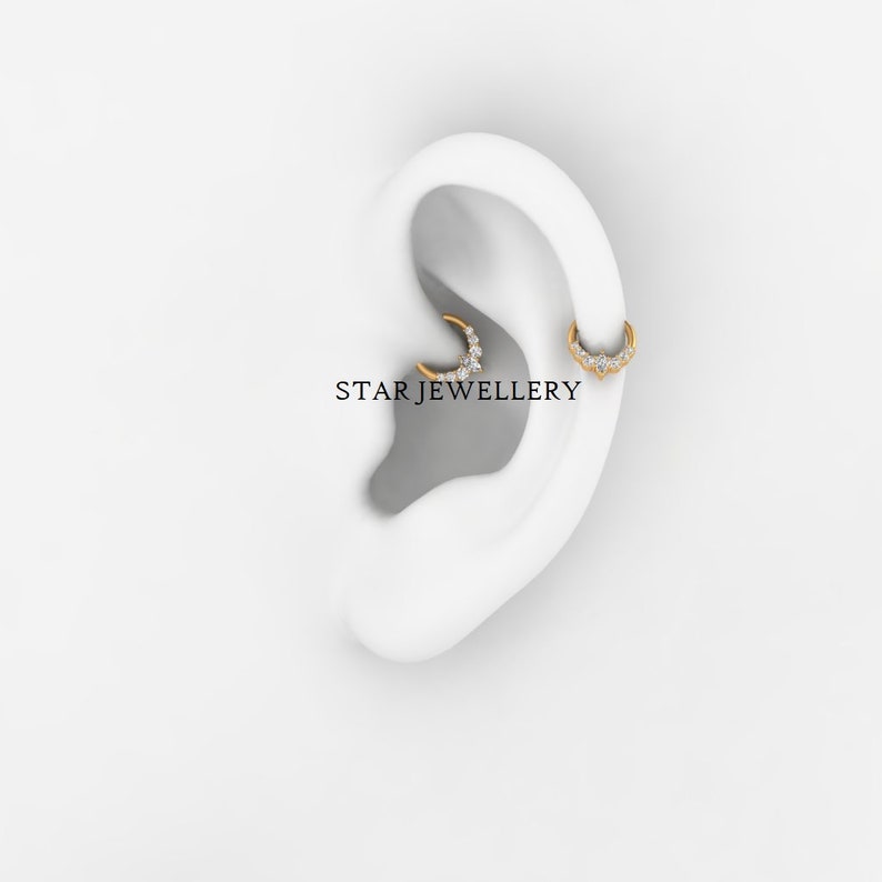 May include: A close-up of a person's ear with two gold hoop earrings with small diamonds. The earrings are in the shape of a crescent moon. The text "STAR JEWELLERY" is visible below the earrings.