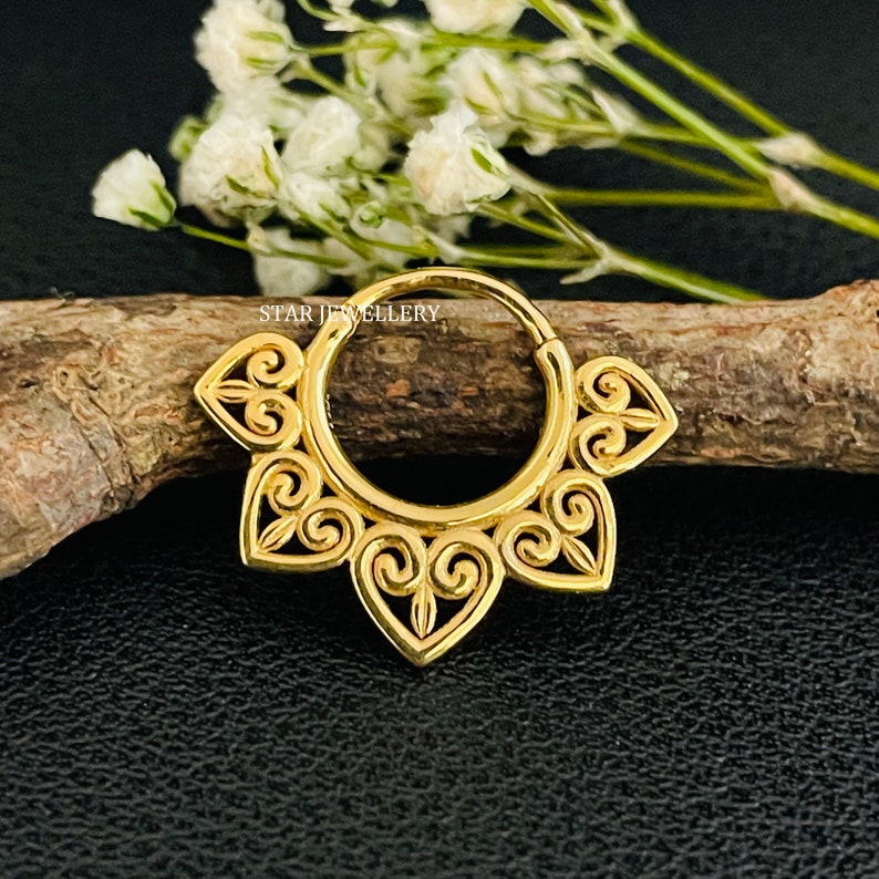 May include: Gold hoop earring with a decorative design featuring intricate swirls and heart shapes. The earring is made of metal and has a polished finish.