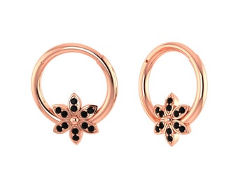 Pode incluir: Um par de brincos de argola de ouro rosa com um amuleto de flor preta. Cada amuleto de flor é adornado com pequenas pedras preciosas pretas.