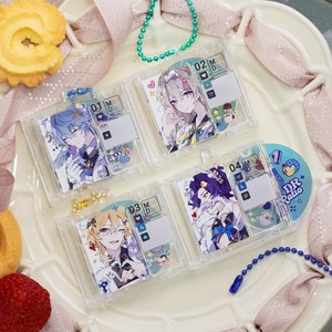 May include: Four clear plastic keychains with colourful anime character illustrations and circular charms. The charms feature a blue and white character, a pink and white character, a yellow and white character, and a blue and purple character. The keychains are on a white plate with a pink ribbon.
