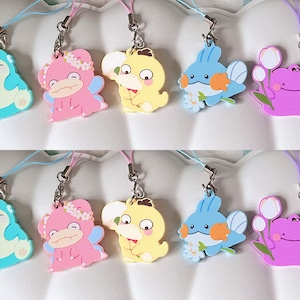 May include: A set of ten colorful keychains featuring cartoon characters. The keychains are made of rubber and have a variety of designs, including a blue and green frog, a pink and white pig, a yellow and white duck, a blue and white fish, and a purple and white ghost. The keychains are attached to silver chains.