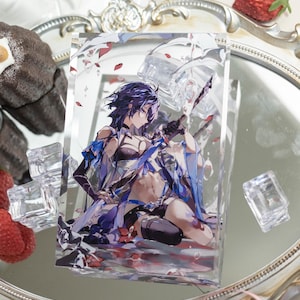 Peut inclure: Un support en acrylique transparent avec une illustration de personnage d'anime coloré à l'intérieur. Le personnage est une femme aux cheveux violets, vêtue d'une tenue bleue et blanche, et tenant une épée. Le support est sur une surface blanche avec des fraises et d'autres objets décoratifs.