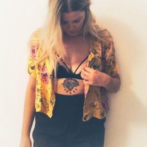 May include: A yellow floral print short-sleeved shirt with pink and green accents. The shirt is paired with black shorts and a black bralette. The image has a vintage aesthetic, with the text "plat_arte" in the bottom left corner.