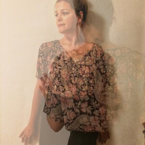 May include: A floral print top with a V-neck and short sleeves, paired with a black skirt. The top features a pattern of pink and black flowers. The image has the text "plat_arte" in the bottom left corner.