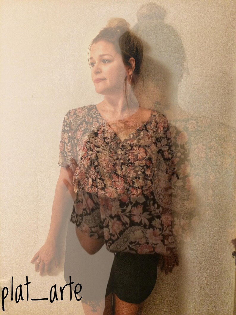 May include: A floral print top with a V-neck and short sleeves, paired with a black skirt. The top features a pattern of pink and black flowers. The image has the text "plat_arte" in the bottom left corner.