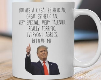 Könnte beinhalten: Weiße Keramik-Tasse mit Henkel. Die Tasse zeigt den Text "YOU ARE A GREAT ESTHETICIAN, GREAT ESTHETICIAN. VERY SPECIAL, VERY TALENTED. REALLY TERRIFIC. EVERYONE AGREES. BELIEVE ME." mit dem Bild eines Mannes, der den Daumen hochhält.