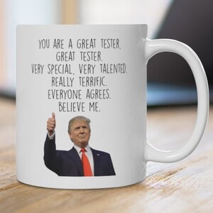 May include: White ceramic mug with a handle. The mug has the text "YOU ARE A GREAT TESTER, GREAT TESTER. VERY SPECIAL, VERY TALENTED, REALLY TERRIFIC, EVERYONE AGREES. BELIEVE ME." and an image of a man giving a thumbs up.