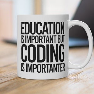 May include: White ceramic mug with the text "EDUCATION IS IMPORTANT BUT CODING IS IMPORTANTER" in black. The mug is on a wooden surface, with a laptop in the background.