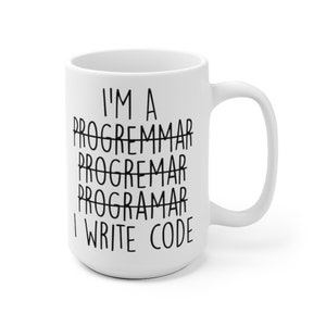 May include: White ceramic mug with a large handle. The mug features the text "I'M A PROGREMMAR PROGREMMAR PROGRAMAR I WRITE CODE" in black, with the word "PROGRAMMAR" crossed out multiple times.