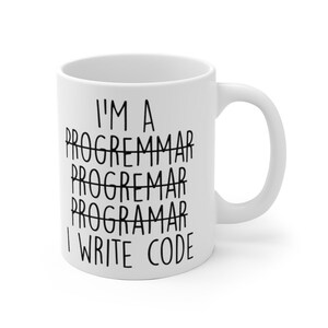 May include: White ceramic mug with a curved handle. The mug features the text "I'M A PROGRAMMAR PROGRAMMAR PROGRAMAR I WRITE CODE" in black, with the word "PROGRAMMAR" crossed out multiple times. A humorous gift for programmers.