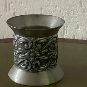 Op de afbeelding: Twee zilveren metalen bekers, een met een versierd ontwerp en de andere met een getextureerd oppervlak.