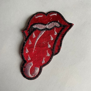 May include: Red and white embroidered patch of a tongue sticking out with a black outline. The tongue has a white design with a black outline.