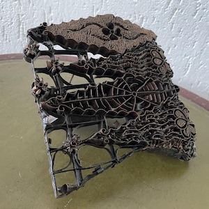 Pode incluir: Um bloco de impressão batik vintage, intrincado e de cor cobre, com um design floral. O bloco é feito de metal e tem um design em relevo.