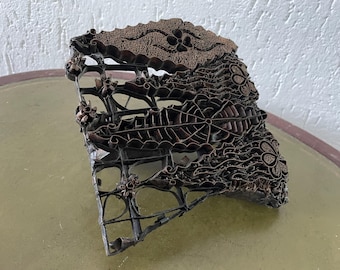 Könnte beinhalten: Ein antiker, filigraner Batikdruckblock aus Kupfer mit einem floralen Muster. Der Block ist aus Metall und hat ein erhabenes Design.
