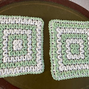 Könnte beinhalten: Zwei gehäkelte quadratische Platzsets in Weiß und Hellgrün. Die Platzsets haben einen gewellten Rand und ein sich wiederholendes Muster aus Spiralen.