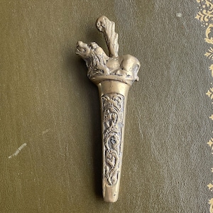 Op de afbeelding: Een vintage messing briefopener met een leeuwenfiguur en sierlijke bloemmotieven. De goudkleurige opener staat tegen een groene achtergrond, wat het gedetailleerde ontwerp benadrukt.