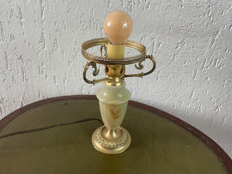 Op de afbeelding: Een groene en gouden tafellamp met een witte glazen kap. De lamp heeft een decoratieve voet en een ronde kap.