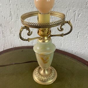 Op de afbeelding: Een groene en gouden tafellamp met een decoratieve voet en een ronde kap. De lamp heeft een witte gloeilamp.