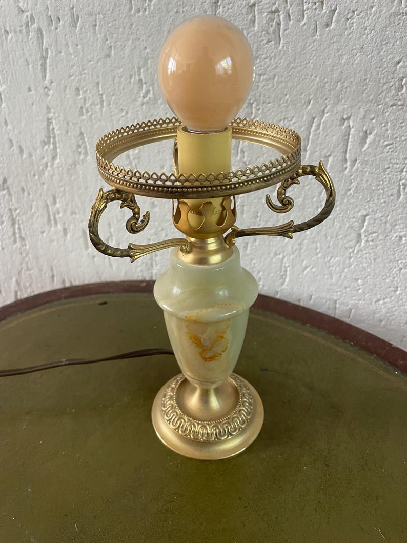Op de afbeelding: Een groene en gouden tafellamp met een decoratieve voet en een ronde kap. De lamp heeft een witte gloeilamp.