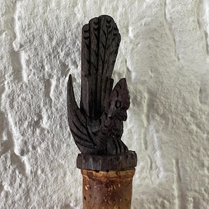 Op de afbeelding: Een donkerbruine houten flessenstop, gesneden in de vorm van een haan met een opgeheven staart.