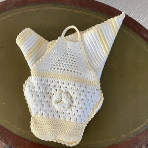 Puede incluir: Un top halter blanco de ganchillo con rayas amarillas. El top tiene un delicado diseño floral en el centro.