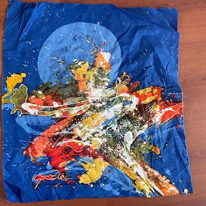 Może przedstawiać: Niebieski kwadratowy kawałek materiału z kolorowym abstrakcyjnym wzorem. Wzór zawiera duże białe koło z żółtym, pomarańczowym i czerwonym abstrakcyjnym wzorem w środku. Tło jest ciemnoniebieskie z białymi plamkami.