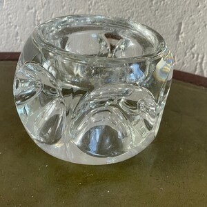 Op de afbeelding: Een glazen kaarsenhouder van helder glas met een getextureerd, bubbelvormig ontwerp. De houder is rond en heeft een brede opening aan de bovenkant.